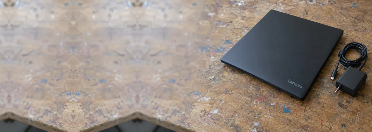 A closed matte black Lenovo laptop with a slim charger and cable on a wooden repair bench