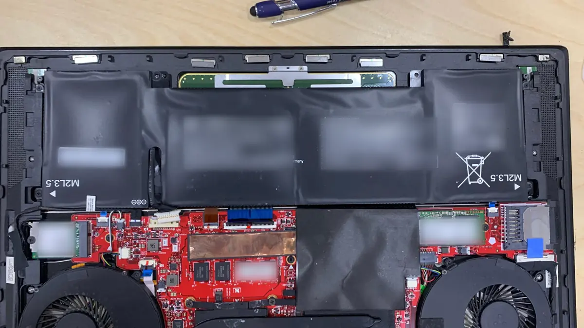 Inside an opened laptop on the bench, with a swollen battery above the mainboard and the cooling fans