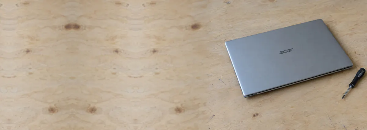 A closed silver Acer laptop beside a screwdriver on a plywood bench