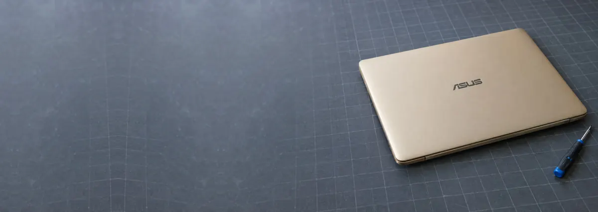 A closed gold-toned ASUS laptop beside a screwdriver on a slate-grey workbench