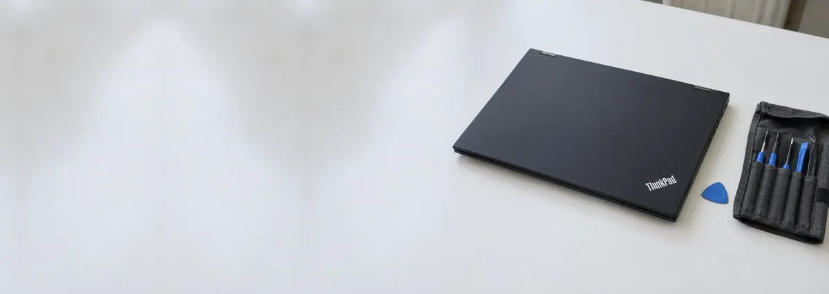 A closed black Lenovo ThinkPad beside an opening pick and a toolkit roll on a white bench
