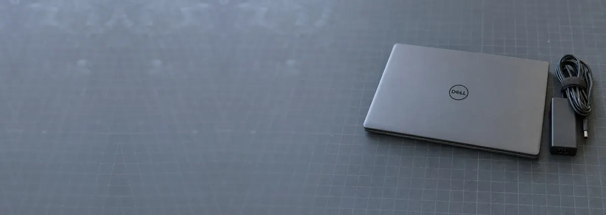 A closed matte-grey Dell laptop beside a charger cable on a slate-grey workbench