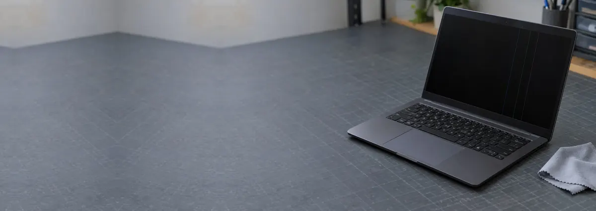 An open laptop with faint vertical lines on its screen beside a cloth on a slate-grey workbench