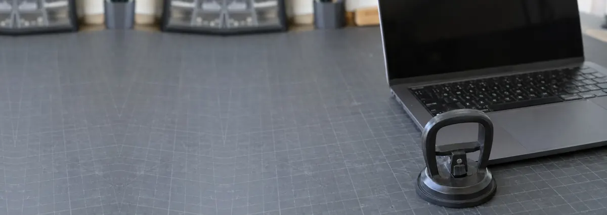 An open dark laptop with its screen off beside a suction handle on a slate-grey workbench