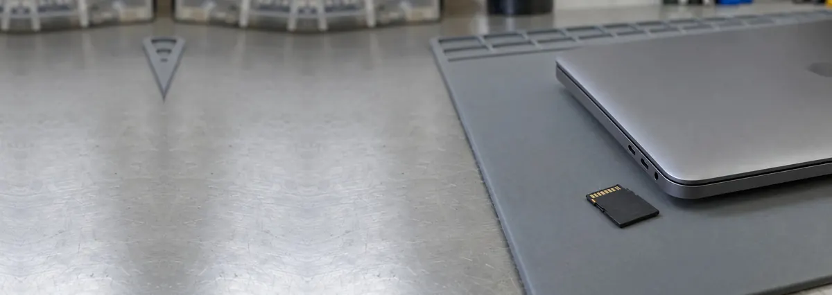 A closed laptop beside an SD card on a grey anti-static mat