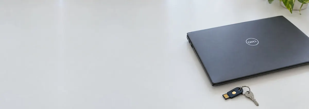 A closed Dell laptop beside a hardware security key on a white bench