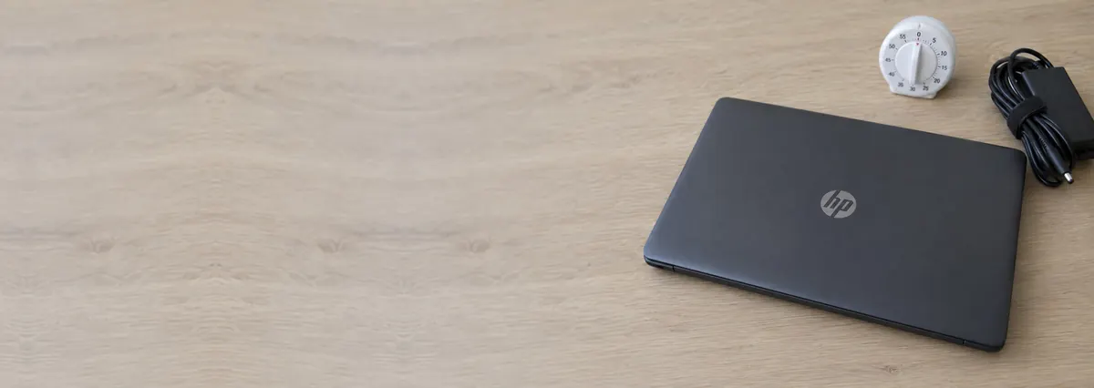 A closed charcoal HP laptop beside a timer and a charger cable on an oak desk top