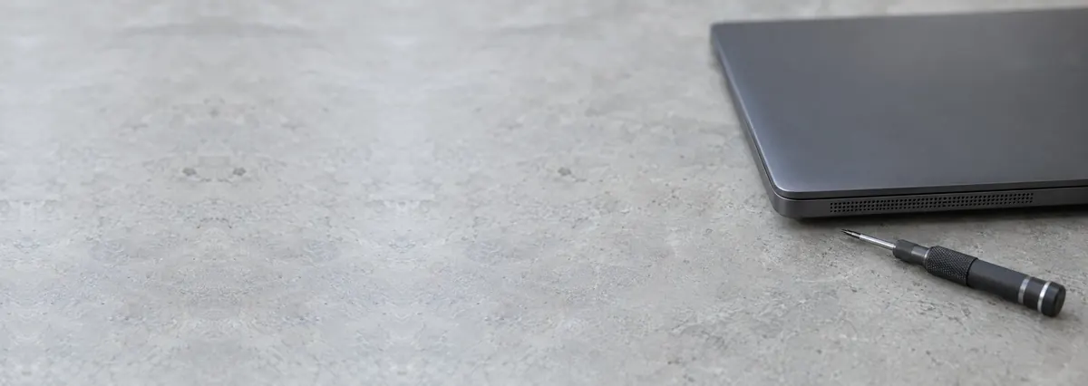 A closed dark laptop with its speaker edge toward the camera beside a screwdriver