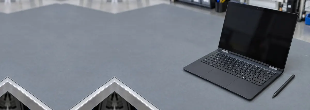 An open black 2-in-1 laptop with a stylus pen beside it on a grey anti-static mat