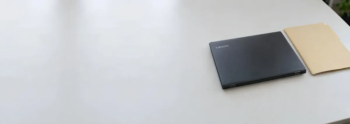 A closed Lenovo laptop beside a closed manila folder on a white bench