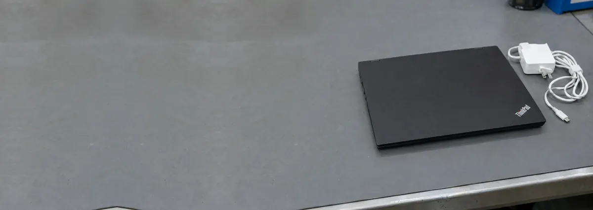A closed black Lenovo ThinkPad laptop beside an unplugged charger on a grey anti-static mat