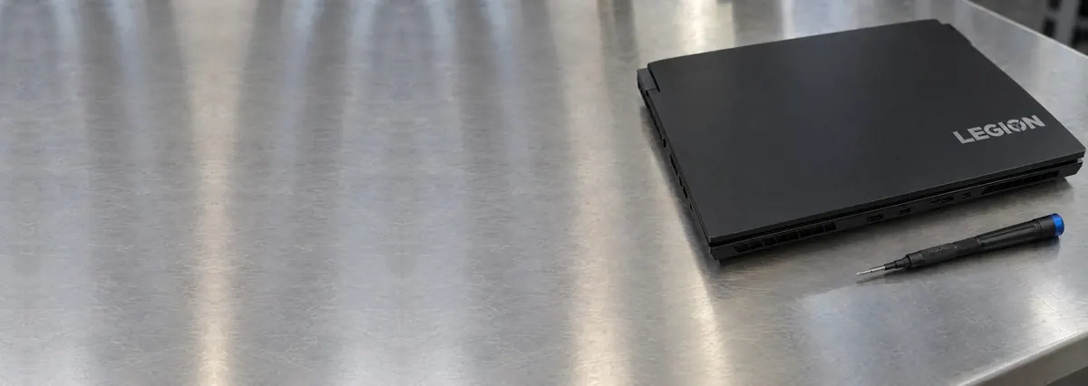 A closed black Lenovo Legion gaming laptop beside a screwdriver on a steel workbench