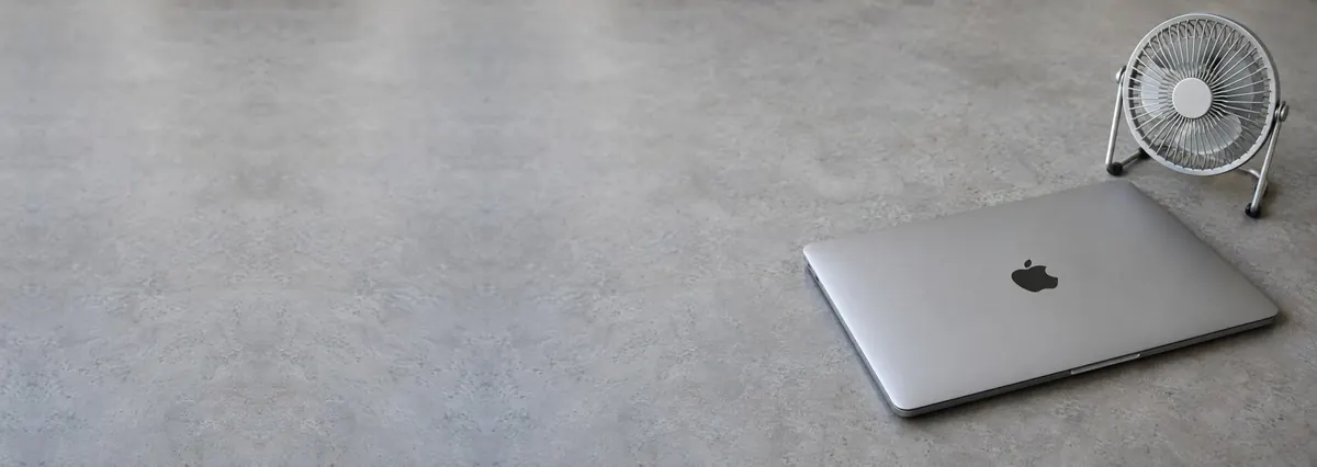 A closed Apple MacBook Pro beside a small desk fan on a concrete-effect workbench