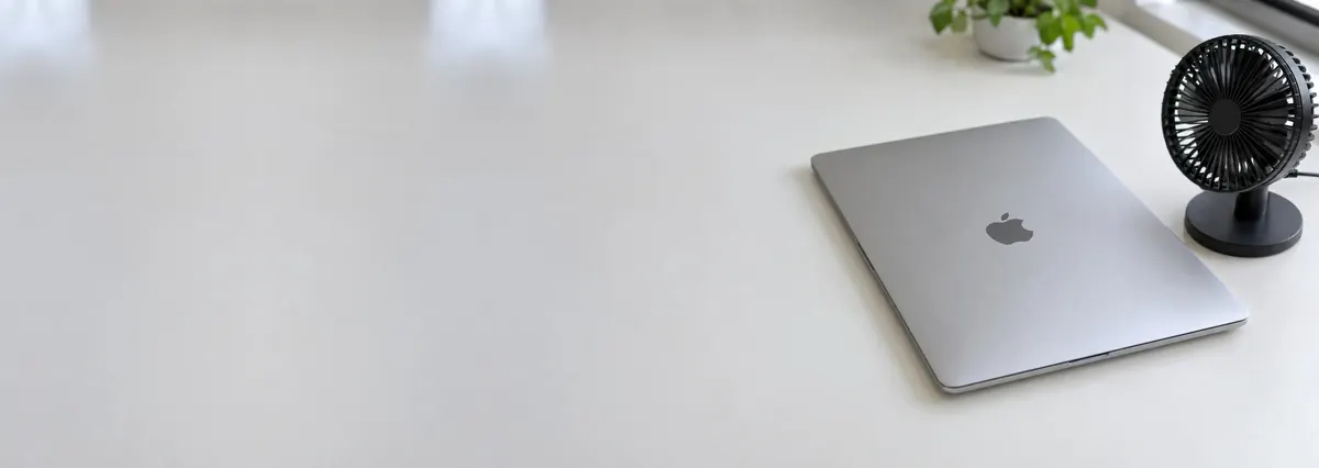 A closed silver Apple MacBook beside a small desk fan on a white bench