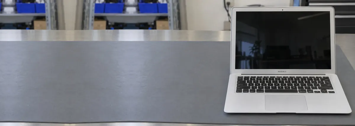 An open silver Apple MacBook with its screen switched off standing on a grey anti-static mat