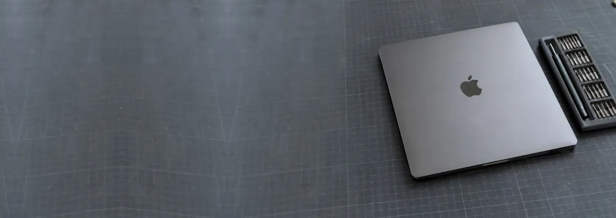 A closed space-grey Apple MacBook Pro beside a precision screwdriver set on a slate-grey workbench