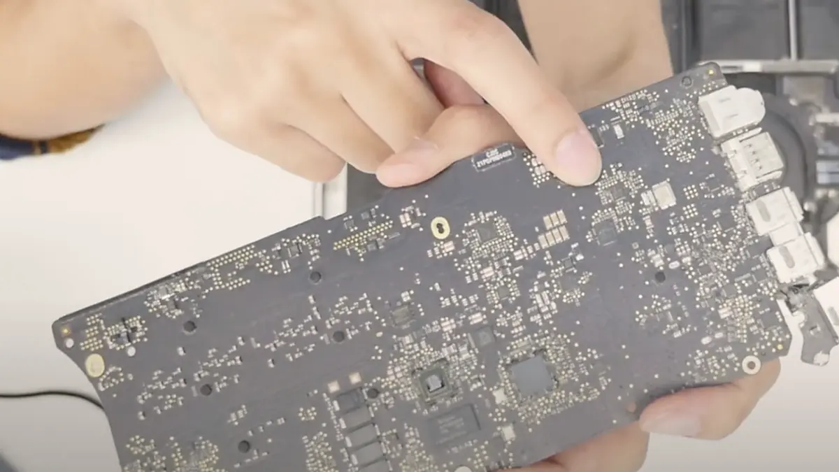 A technician holding a MacBook logic board