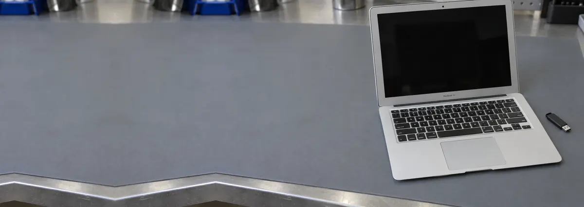 An open silver Apple MacBook with its screen off beside a flash drive on a grey anti-static mat