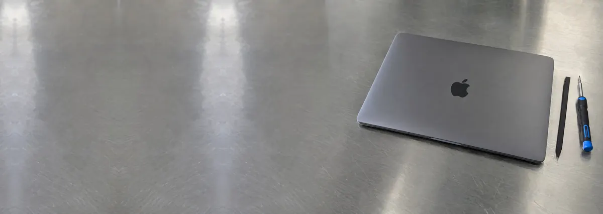 A closed space-grey Apple MacBook Pro beside a spudger and a screwdriver on a steel workbench