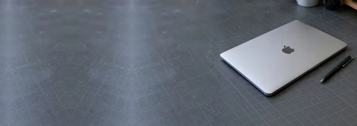 A closed thin silver-grey Apple MacBook beside a pen on a slate-grey workbench