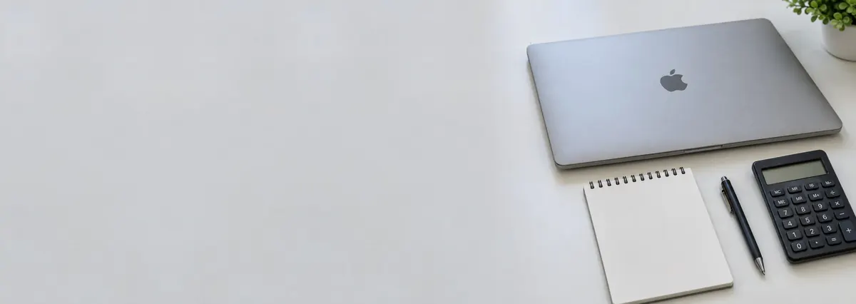 A closed Apple MacBook beside a notepad, a pen and a calculator on a white bench