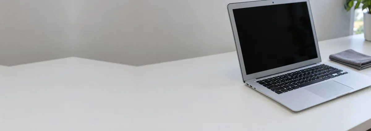 An open silver Apple MacBook with its screen switched off beside a lint-free cloth on a white bench
