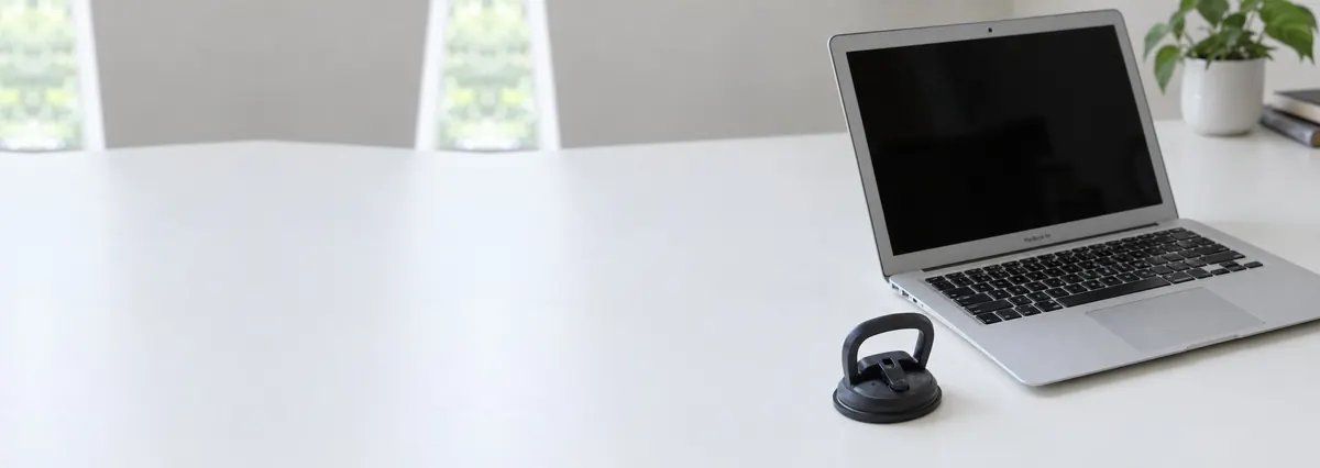 An open silver Apple MacBook with its screen switched off beside a suction handle on a white bench