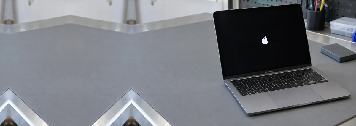 An open Apple MacBook whose screen shows only the Apple logo on a grey anti-static mat