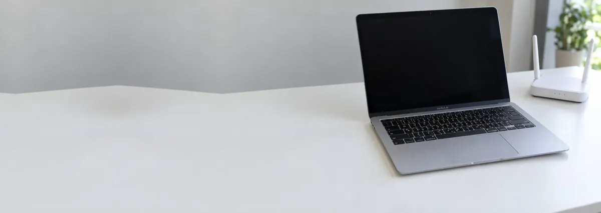 An open silver Apple MacBook with its screen off beside a small wifi router on a white bench