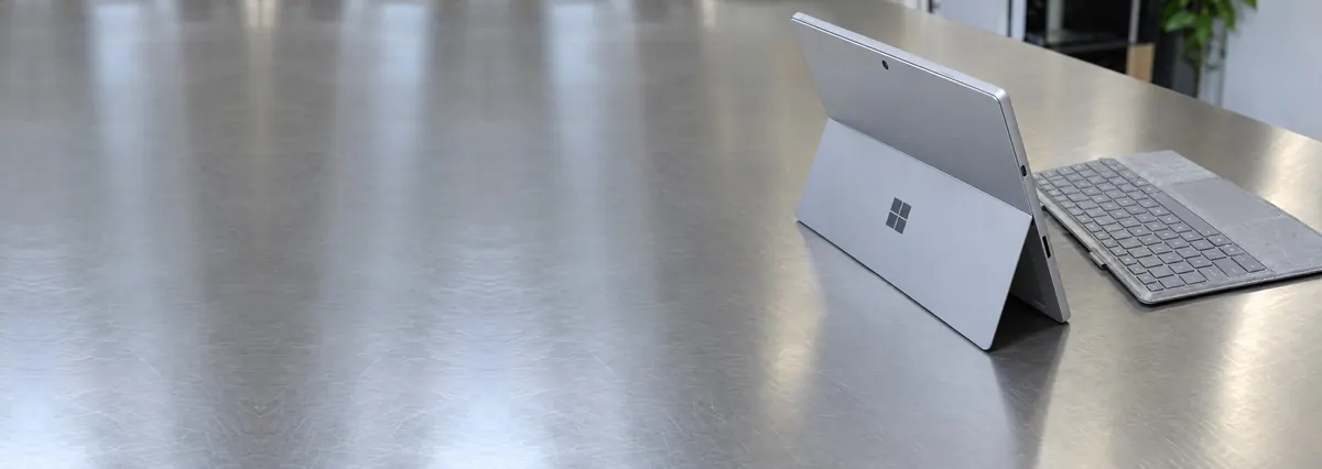 A Microsoft Surface Pro on its kickstand beside a fabric keyboard cover on a steel workbench