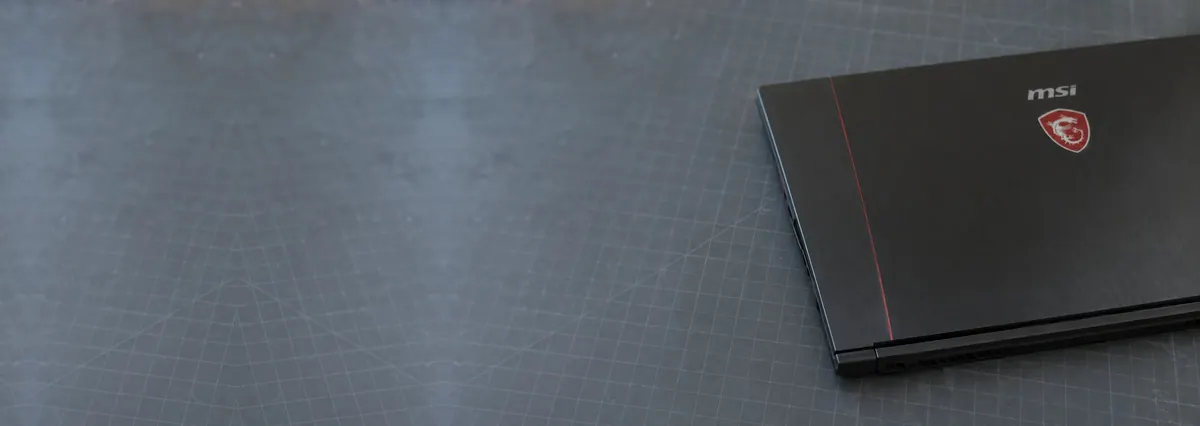 A closed black MSI gaming laptop with a thin red accent on a slate-grey workbench