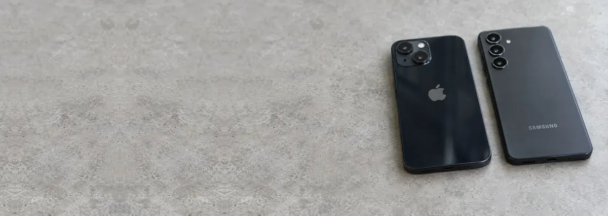 An Apple iPhone and a Samsung Galaxy phone lying face-down on a concrete-effect workbench