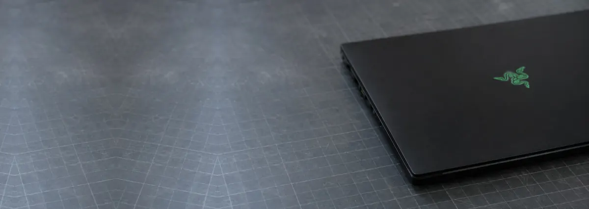A closed black Razer Blade gaming laptop with a matte lid on a slate-grey workbench