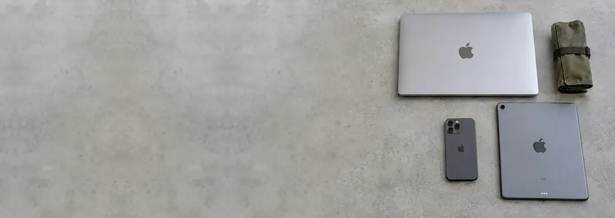 A closed Apple MacBook, an iPhone, an iPad and a toolkit roll on a concrete-effect workbench