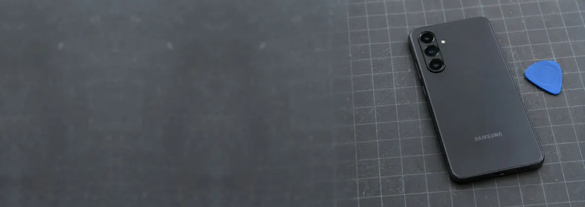 A Samsung Galaxy phone lying face-down beside an opening pick on a slate-grey workbench