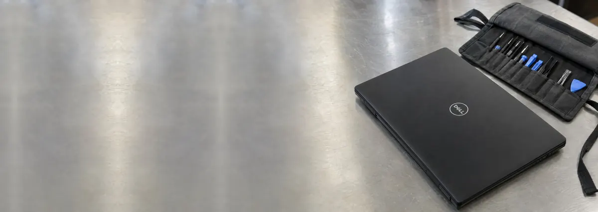 A closed black Dell laptop beside a partly unrolled toolkit roll on a steel workbench