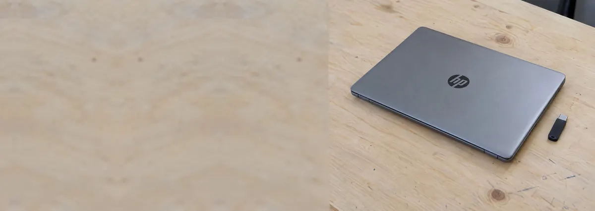 A closed HP laptop beside a USB flash drive on a plywood bench