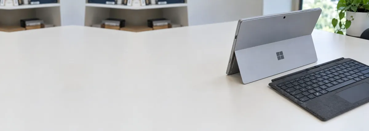 A Microsoft Surface Pro on its kickstand beside a fabric keyboard cover on a white bench